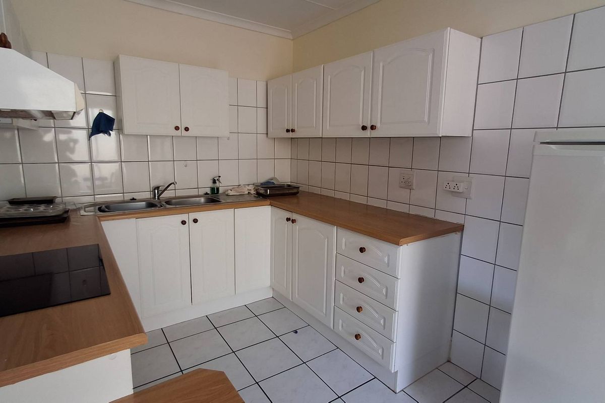 A functional kitchen featuring white cabinetry, laminate countertops, a double basin sink, and a tiled backsplash with a built-in electric hob and extractor fan.