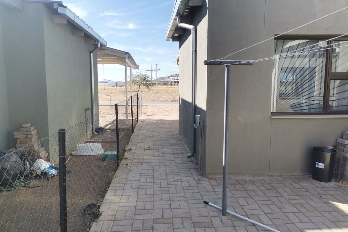 A paved side walkway between two building structures, featuring a metal clothesline and perimeter wire fencing.