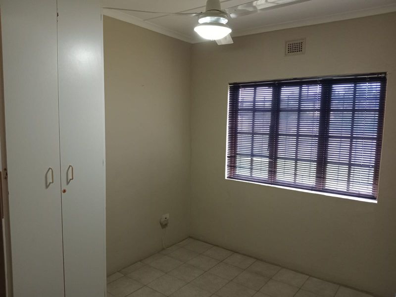 A clean, empty bedroom featuring built-in cupboards, tiled flooring, a ceiling fan, and a window fitted with blinds.