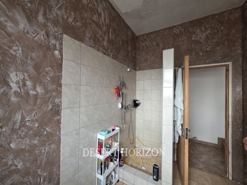 A bathroom featuring a tiled shower enclosure with a mixer, textured wall finishes, and tiled flooring, requiring some maintenance to the ceiling and wall base.