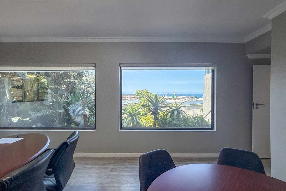 A bright room featuring large windows with views of the surrounding greenery and distant ocean, providing natural light and a pleasant outlook.
