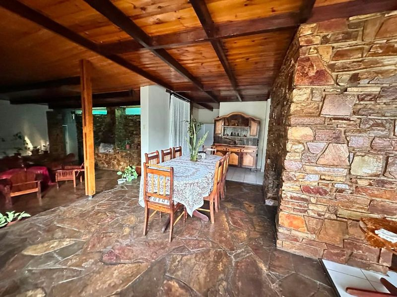 Spacious dining area featuring rustic flagstone flooring, a prominent natural stone fireplace, and an exposed timber beam ceiling.