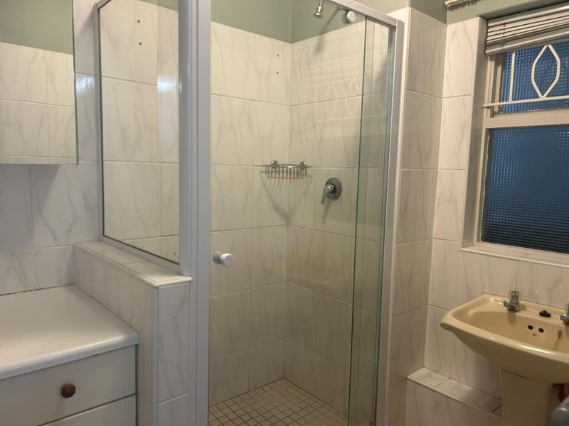 A functional bathroom featuring a glass-enclosed shower, pedestal basin, and tiled finishes, currently requiring minor repairs and cosmetic updates.