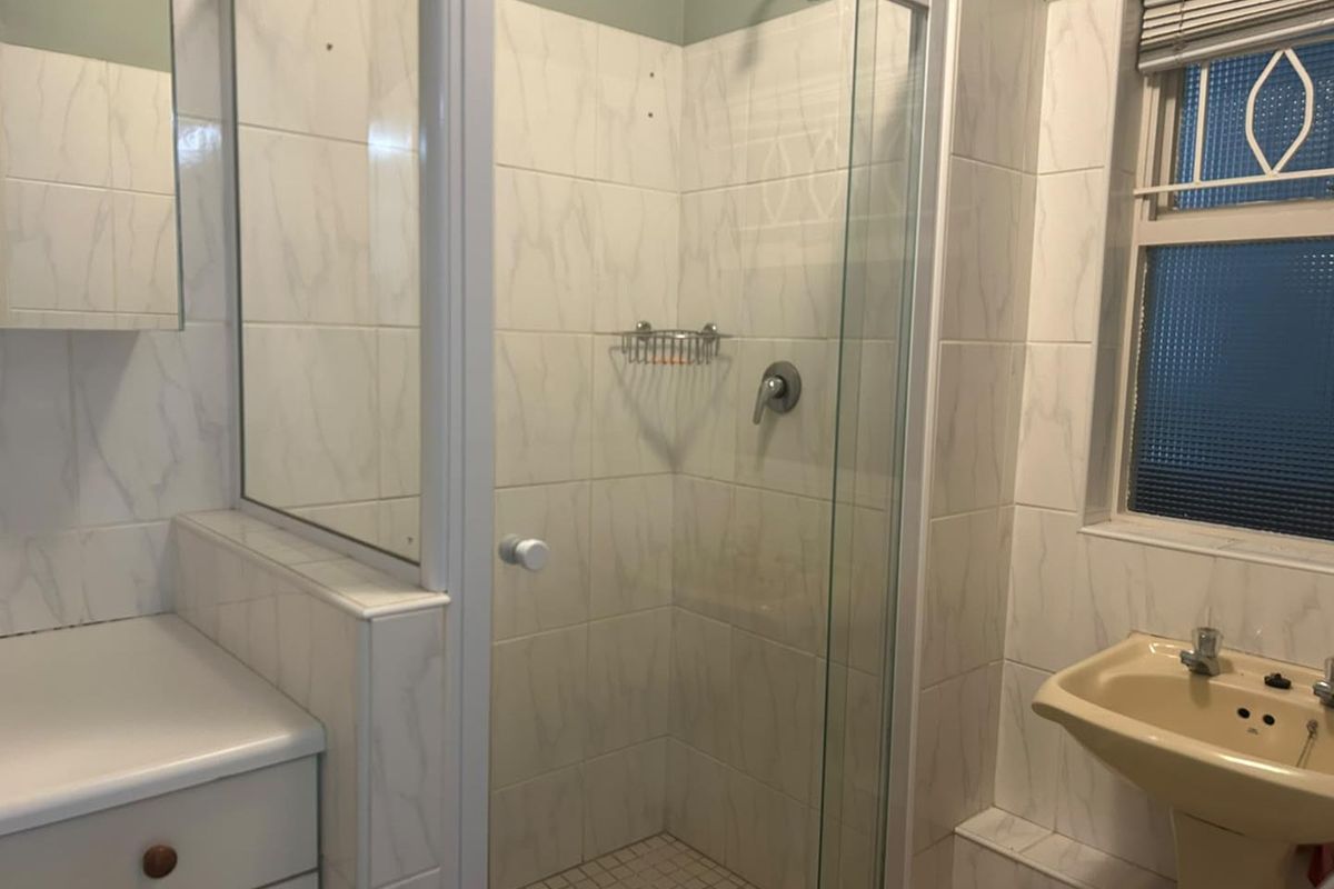 A functional bathroom featuring a glass-enclosed shower, pedestal basin, and tiled finishes, currently requiring minor repairs and cosmetic updates.