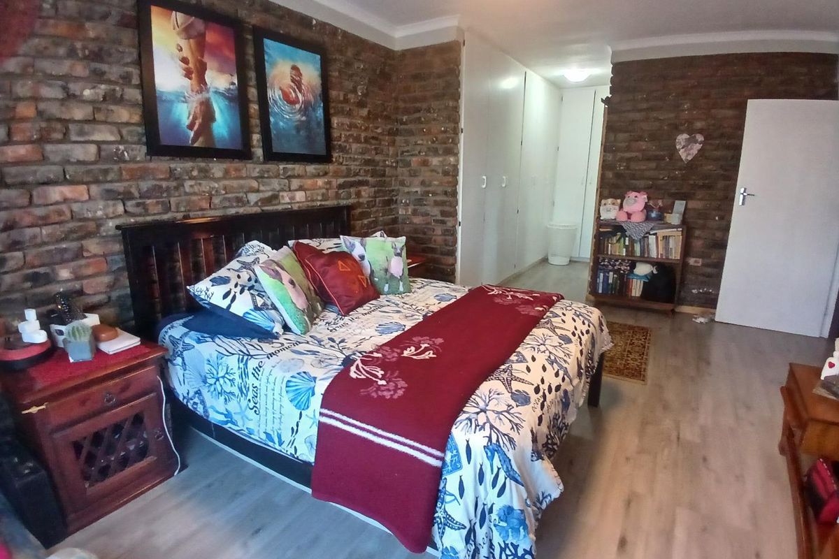 Spacious bedroom featuring a rustic exposed brick feature wall, light wood-look flooring, and built-in cupboards for storage.