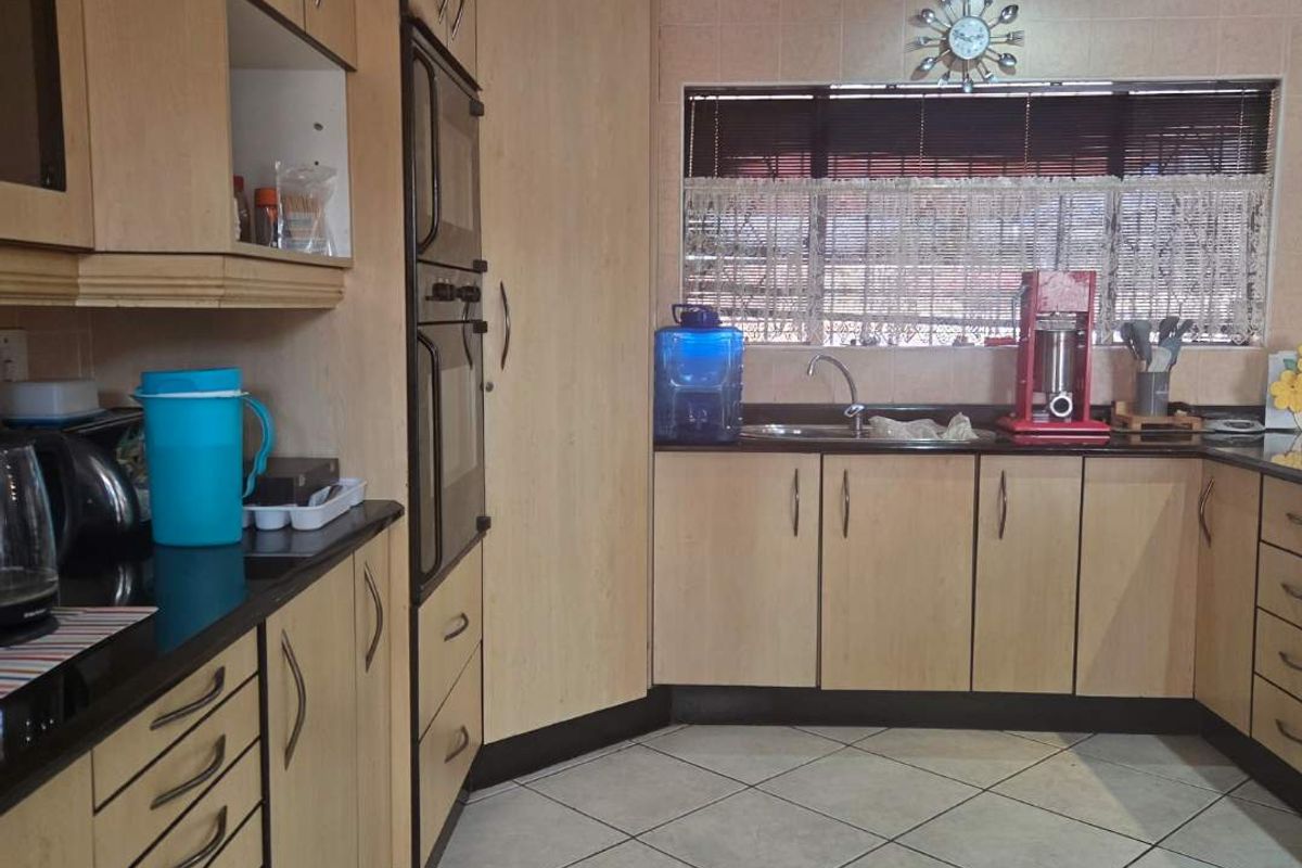 A functional kitchen featuring light wood-finish cabinetry, dark laminate countertops, built-in oven, and tiled flooring with a neutral backsplash.