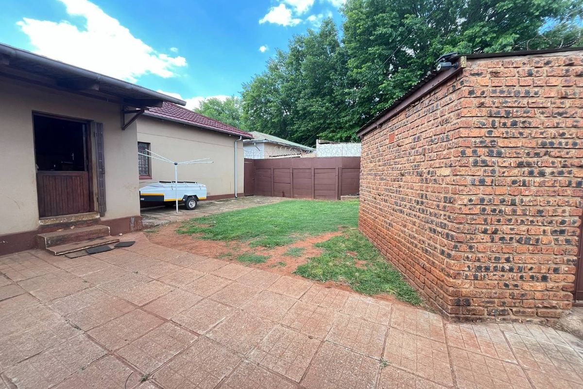 Rear exterior view featuring a paved patio area, a small lawn, and a brick outbuilding with a security camera.