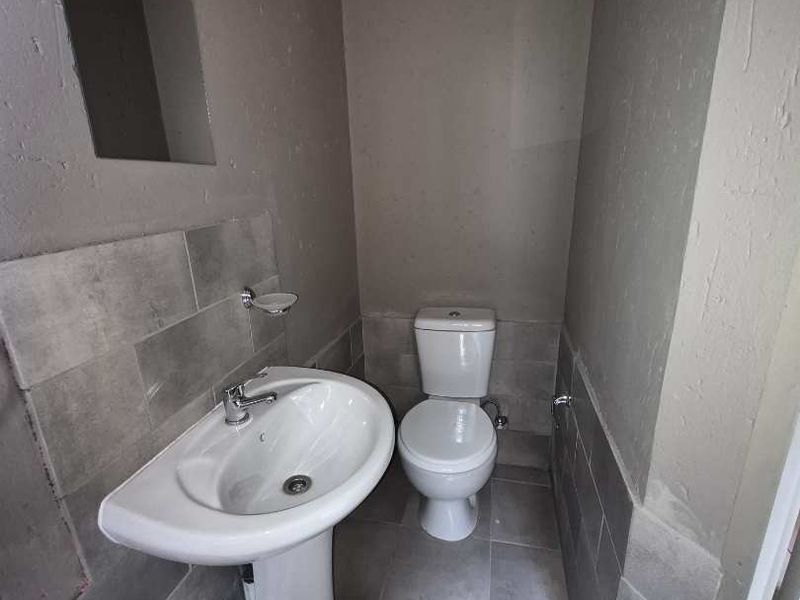 A compact bathroom featuring a pedestal washbasin, toilet, and partial wall tiling. The space requires finishing touches to the walls to improve its overall condition.