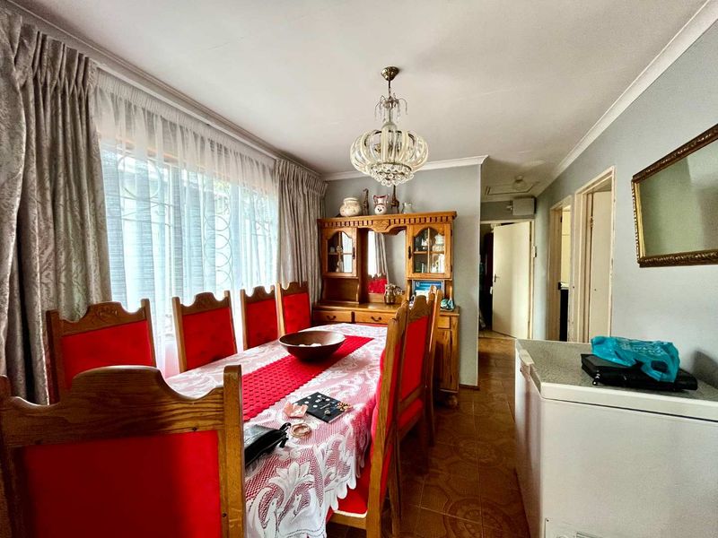 A traditional dining room featuring tiled flooring, a decorative crystal chandelier, and large windows with security bars, offering a functional space for family meals.