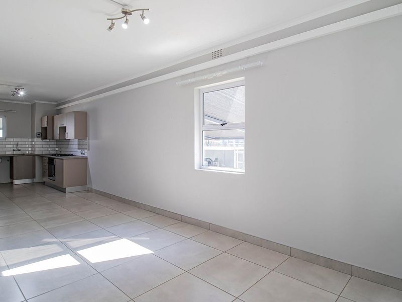 Spacious open-plan living area featuring neutral tiled flooring, a modern kitchen with subway tile backsplash, and ample natural light.