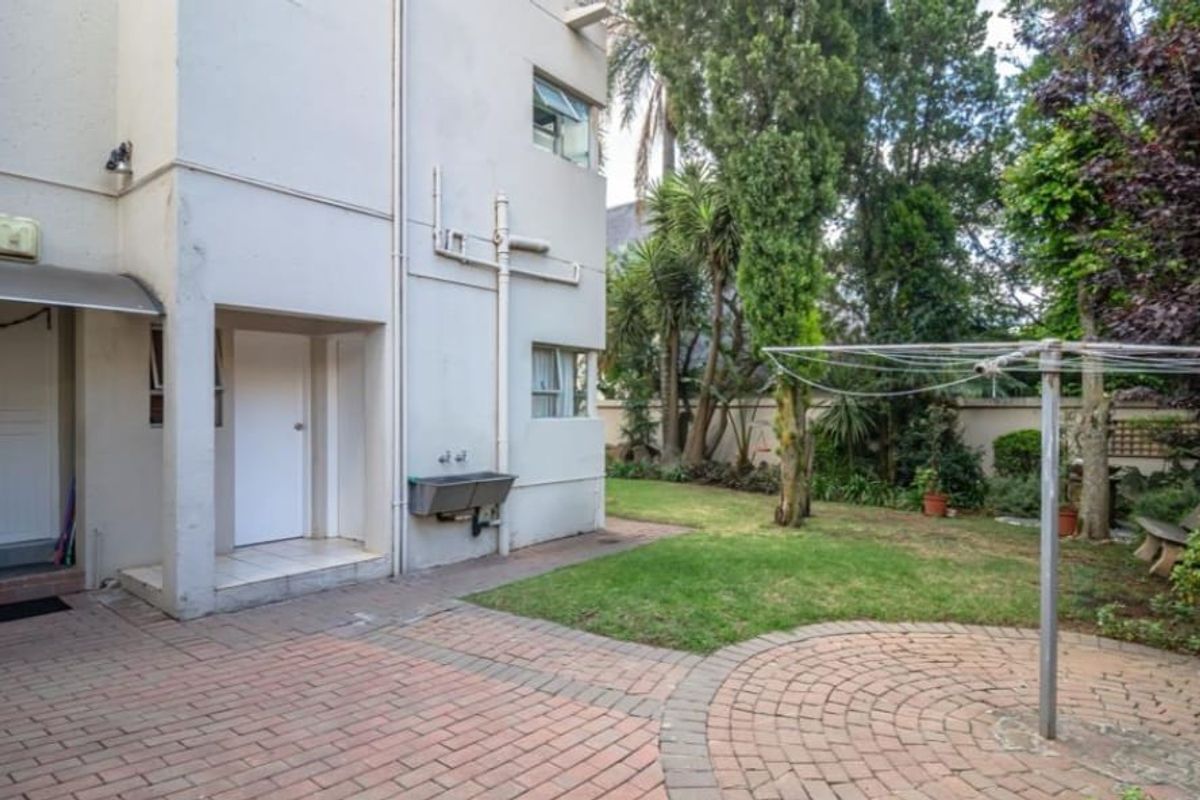 Rear exterior view featuring a paved patio area, a utility sink, and a private garden space with established trees and boundary walls.