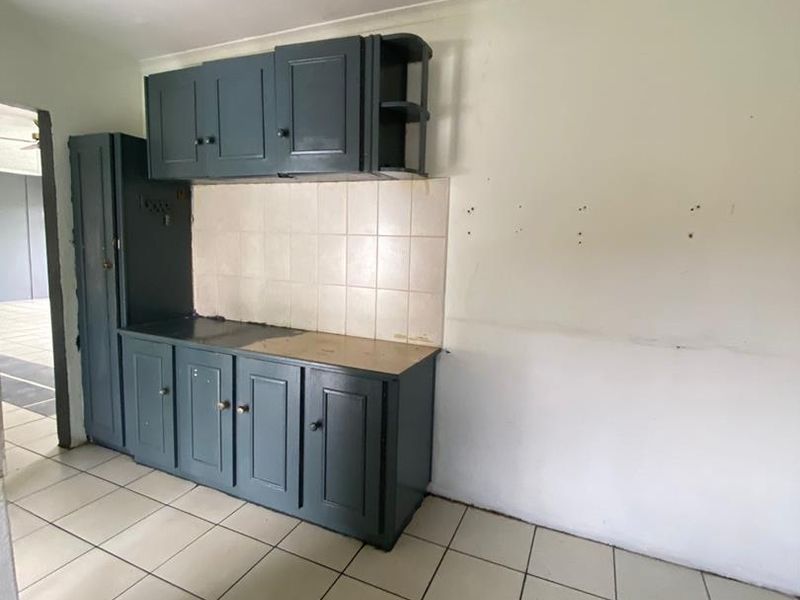 A dated kitchen area featuring dark blue built-in cabinetry, tiled splashback, and tiled flooring, currently requiring renovation and completion of the countertop and wall finishes.