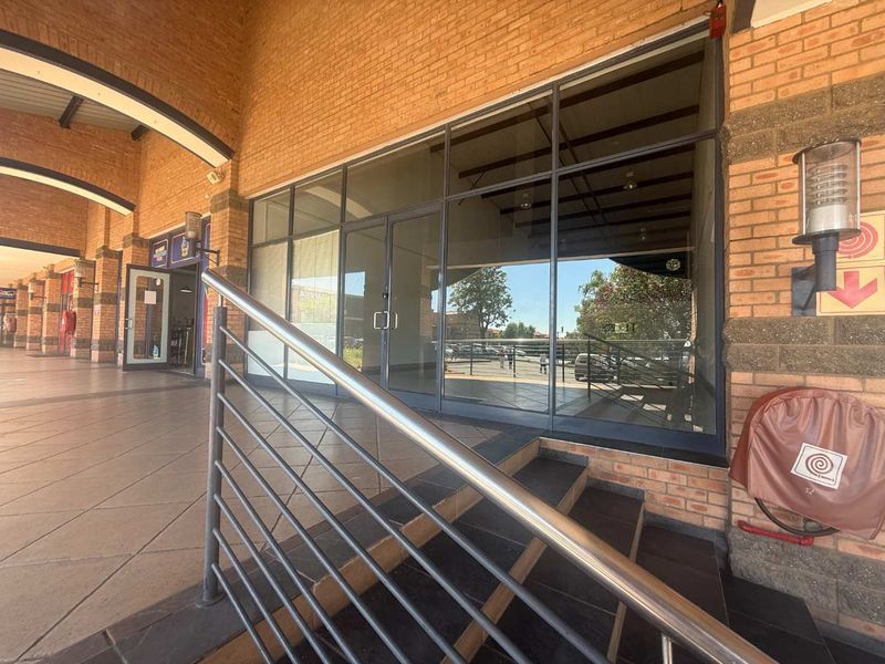 Retail storefront entrance featuring a brick facade, large glass display windows, and tiled steps with a stainless steel handrail.