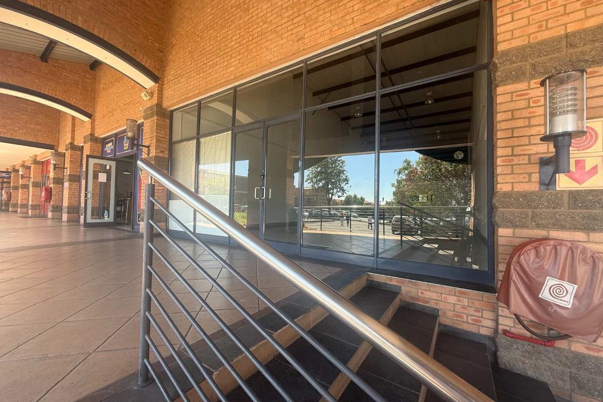 Retail storefront entrance featuring a brick facade, large glass display windows, and tiled steps with a stainless steel handrail.