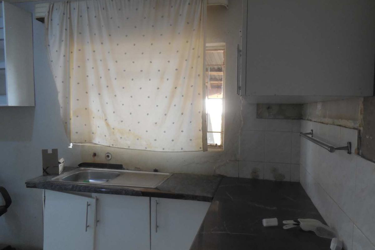 A dated kitchen space featuring built-in cabinetry, laminate countertops, and a stainless steel sink, requiring significant renovation and cosmetic updates.