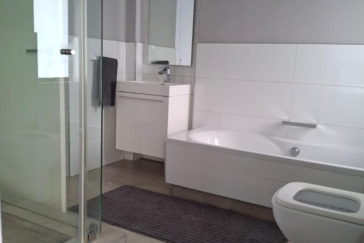 Modern bathroom featuring a glass shower enclosure, built-in bathtub, vanity with basin, and neutral wall tiling.