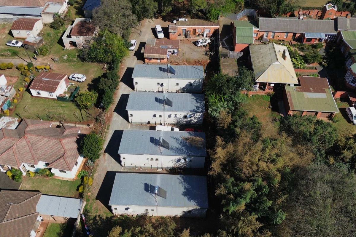Aerial view of a residential property complex featuring multiple units with corrugated metal roofs and installed solar water heating systems.