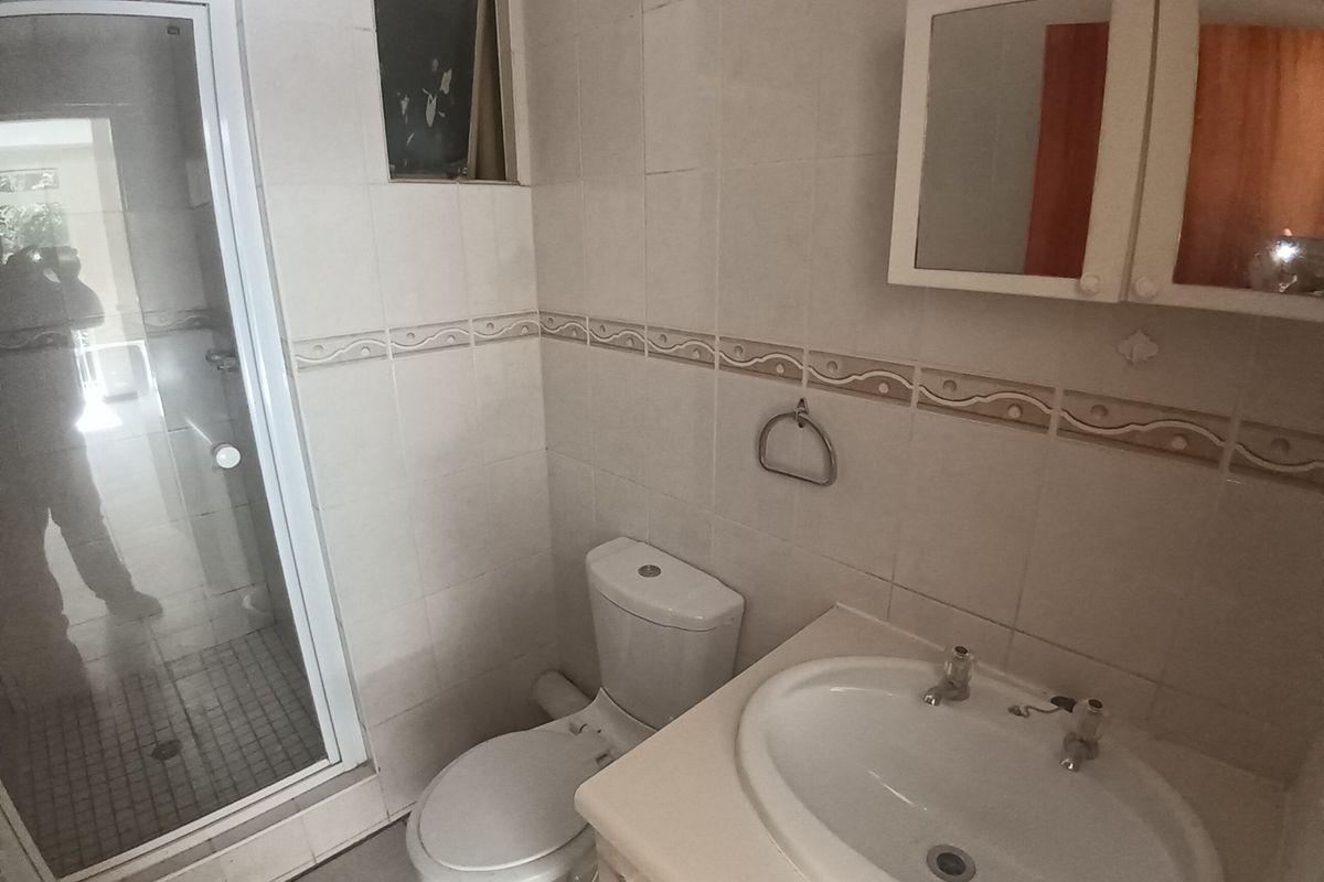 A functional bathroom featuring a shower enclosure, toilet, and vanity basin with wall-mounted storage, requiring some cosmetic updates to the finishes.