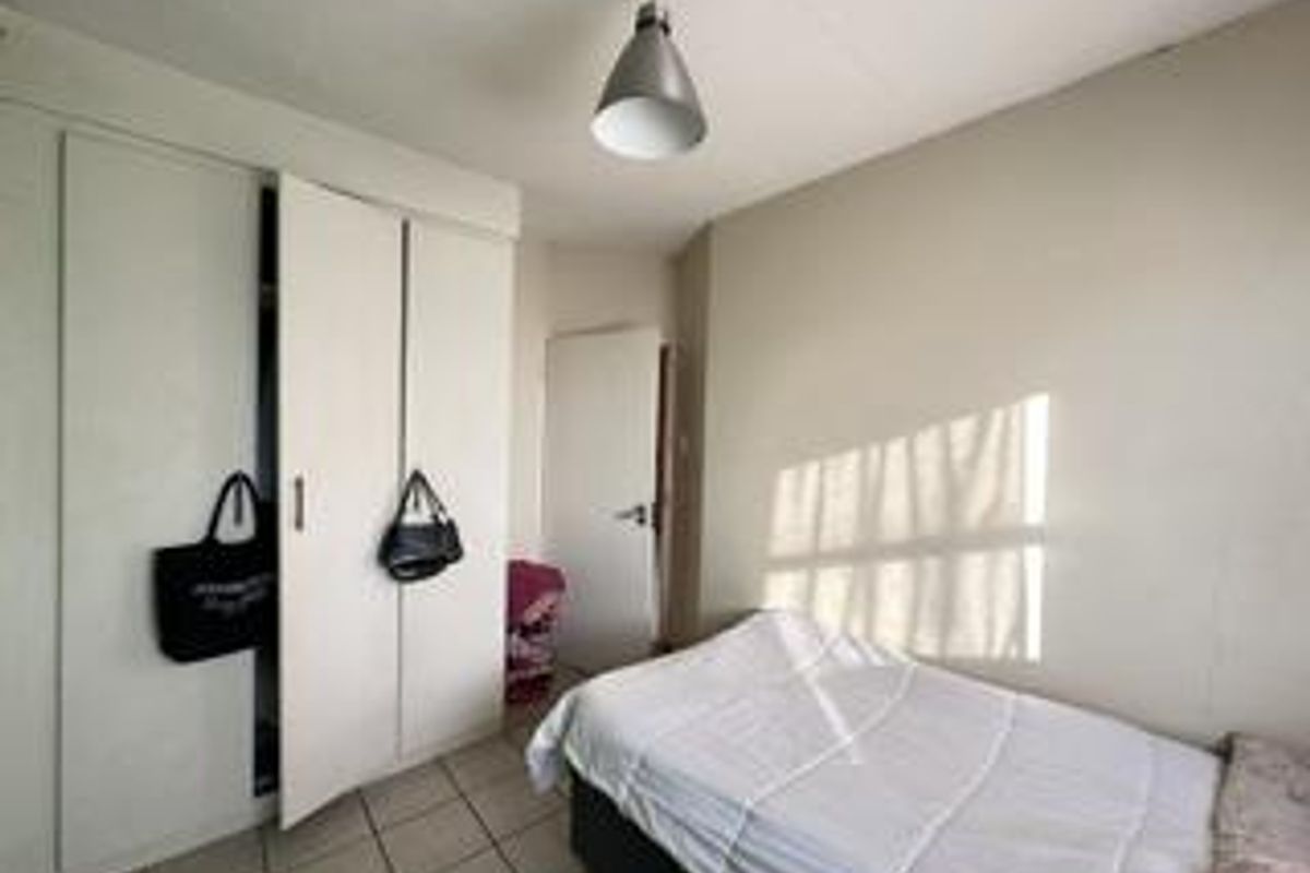 A functional bedroom featuring built-in cupboards, tiled flooring, and a simple pendant light fixture, offering a clean and neutral space.