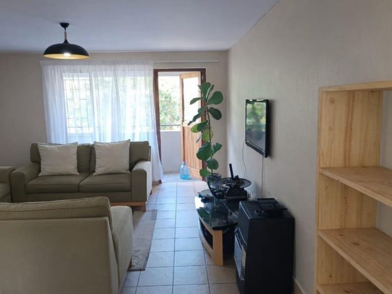 A bright living room featuring tiled flooring, a pendant light, and direct access to an outdoor balcony area through a sliding door.