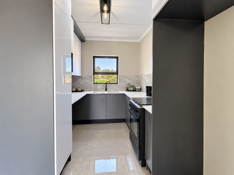Modern kitchen featuring sleek grey and white cabinetry, stone countertops, marble-look backsplash, and high-quality tiled flooring with a functional layout.