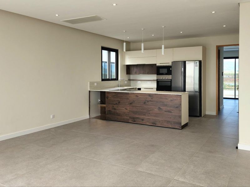 Modern open-plan kitchen featuring two-tone cabinetry, stone countertops, and integrated appliances, set within a spacious living area with large format floor tiles.