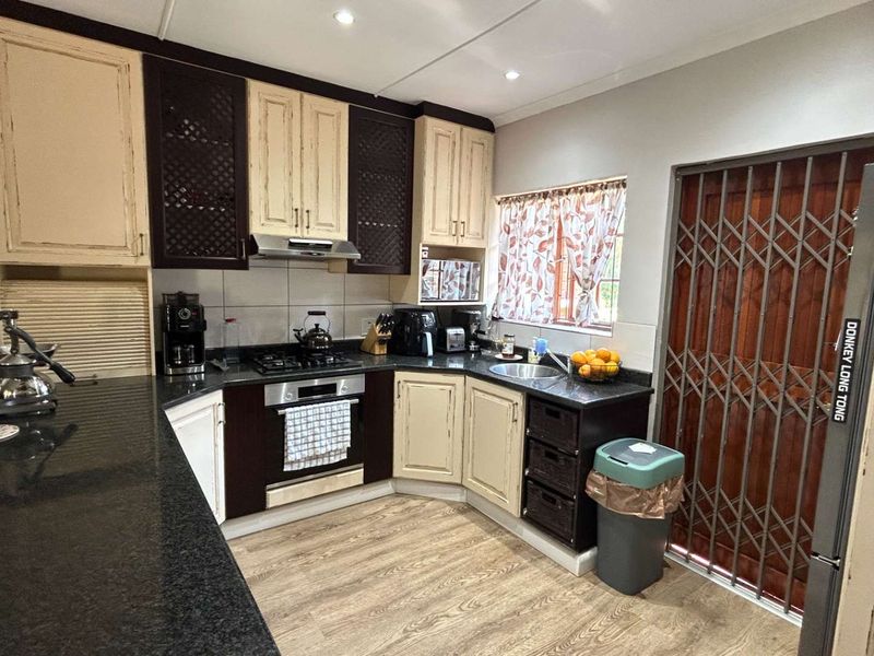 A functional kitchen featuring dark and cream cabinetry, granite countertops, built-in oven and hob, and a secure metal gate leading to the exterior.