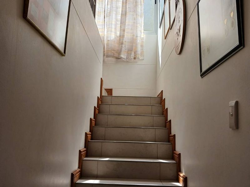 A well-lit staircase featuring tiled steps with wooden trim, leading to an upper level with natural light from a window.