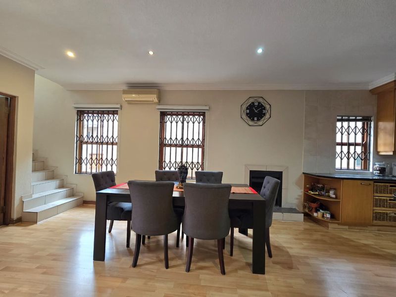 Open-plan living and dining area featuring laminate flooring, a built-in fireplace, split-system air conditioning, and direct access to a tiled staircase.