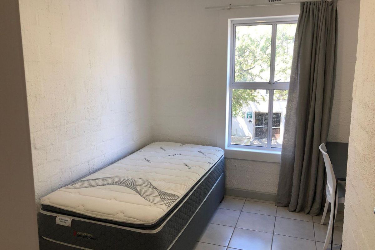 A compact bedroom featuring tiled flooring, a single window with curtain track, and textured wall finishes.