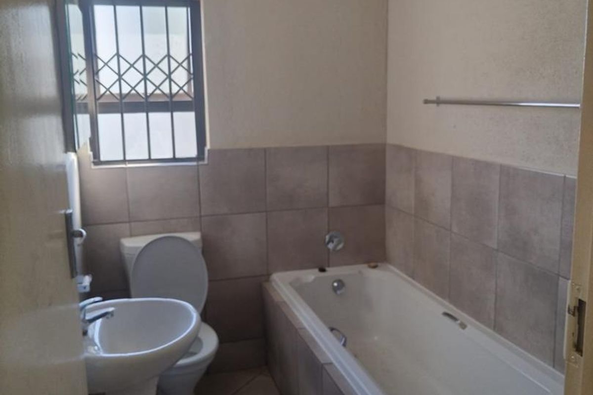 A functional bathroom featuring a pedestal basin, toilet, and a built-in bathtub with tiled splashbacks and flooring.