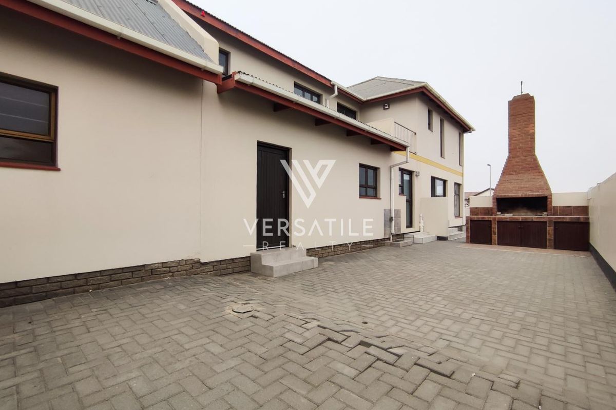 Rear exterior view of the townhouse featuring a paved courtyard, built-in brick braai area, and access doors to the main dwelling.