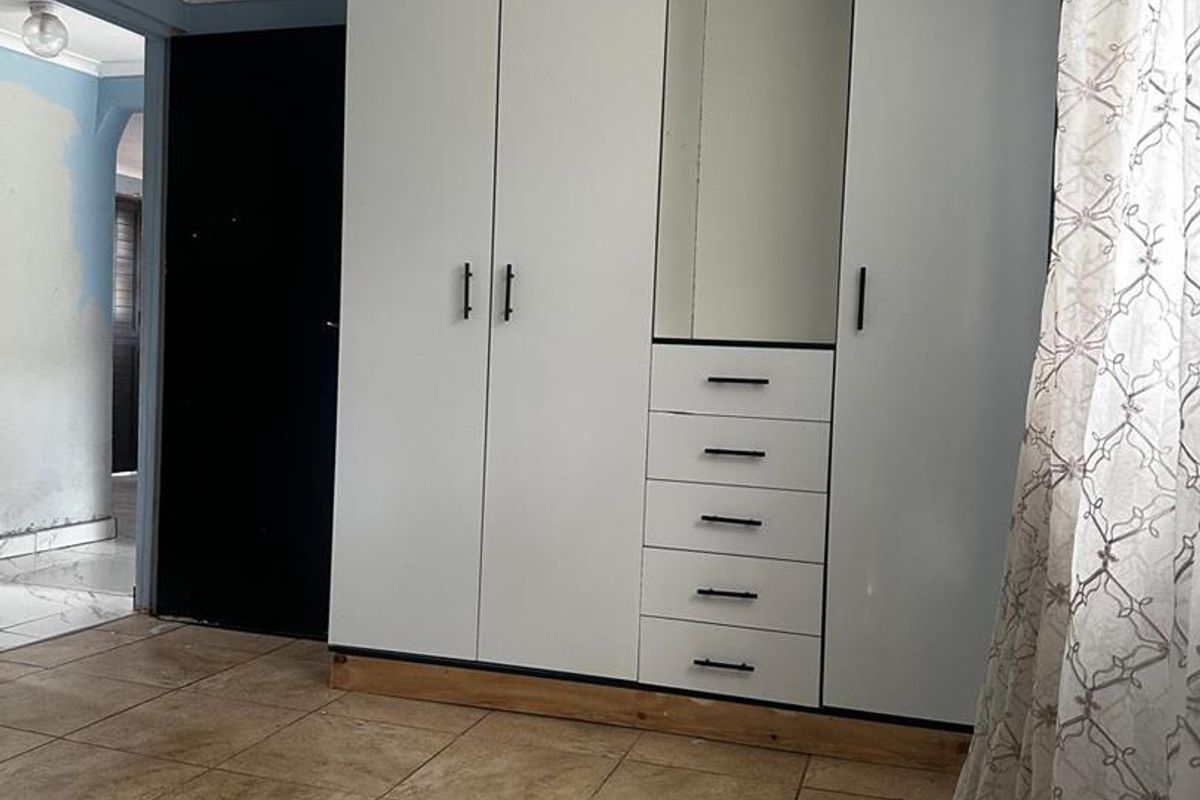 Bedroom featuring built-in white cabinetry with integrated drawers and shelving, tiled flooring, and access to an adjacent hallway.