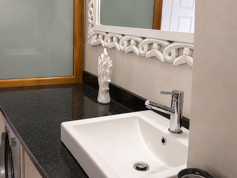 A modern bathroom vanity featuring a dark granite countertop, a sleek white basin with a chrome faucet, and a decorative framed mirror.