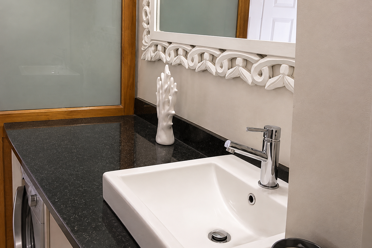 A modern bathroom vanity featuring a dark granite countertop, a sleek white basin with a chrome faucet, and a decorative framed mirror.