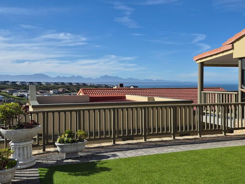 Elevated outdoor terrace featuring a paved patio, artificial lawn, and balustrade, offering expansive coastal and mountain views.