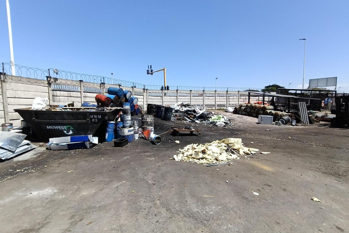 Industrial yard area featuring a concrete surface, perimeter wall with security razor wire, and designated space for waste management and storage.