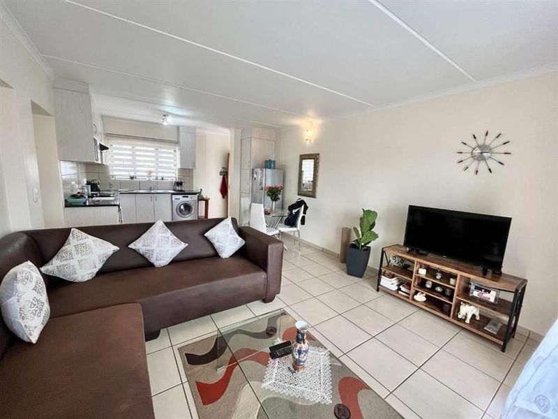 Open-plan living area featuring tiled flooring and a functional kitchen with built-in cabinetry, integrated appliances, and laundry plumbing connections.