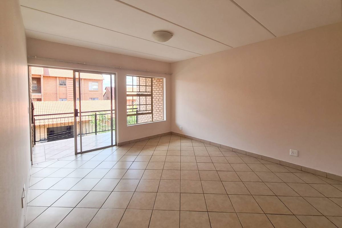 A bright, empty living room featuring tiled flooring, large windows, and a sliding glass door leading to an outdoor balcony area.