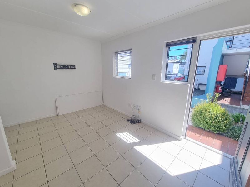 An empty, tiled living room featuring a wall-mounted TV bracket, security bars on the windows, and direct access to an outdoor area.