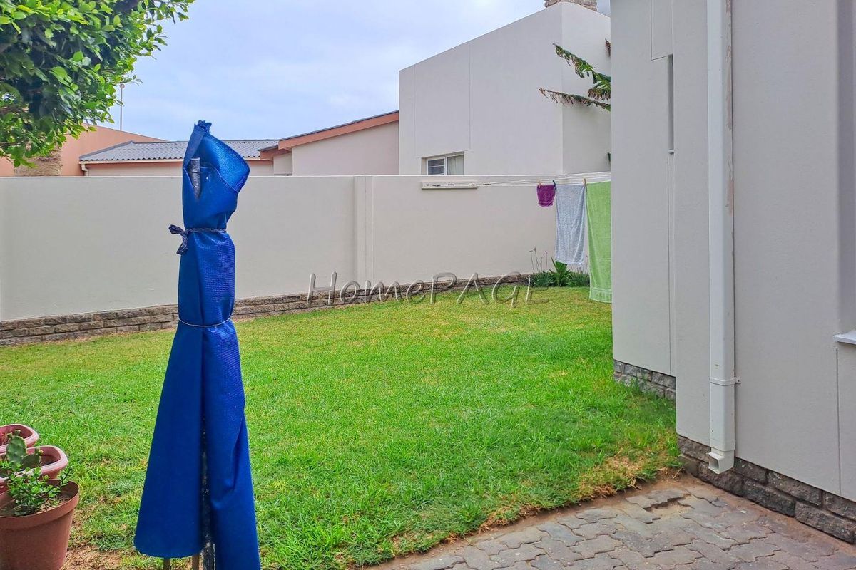 A private rear garden area featuring a lawn, perimeter boundary walls, and paved access, providing a functional outdoor space for the townhouse.