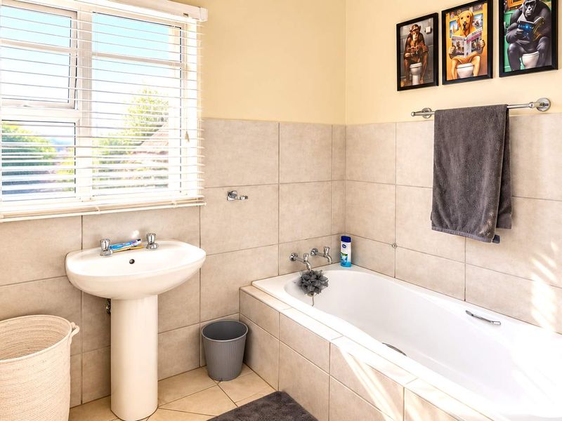 A clean and functional bathroom featuring a pedestal washbasin, a built-in bathtub with tiled surround, and neutral wall tiling.