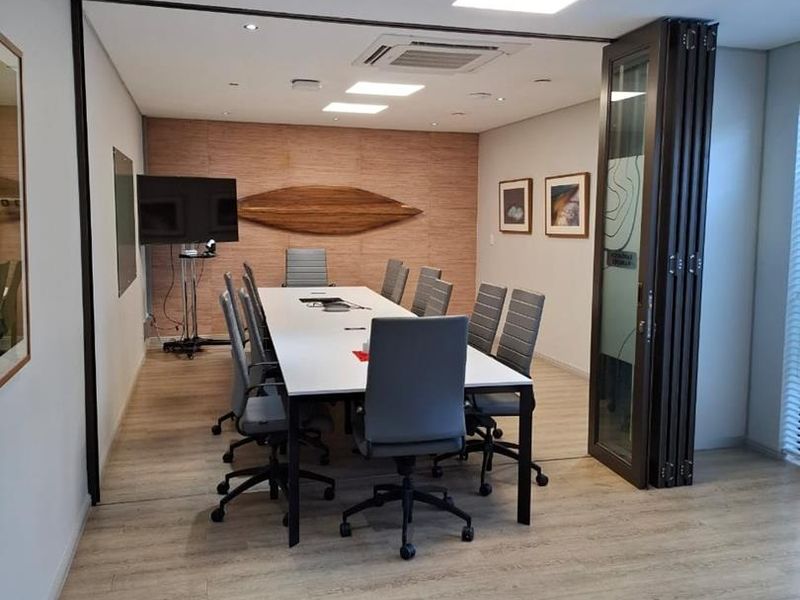 A professional office meeting room featuring a wood-look laminate floor, recessed ceiling lighting, ducted air conditioning, and a modern wood panel feature wall.