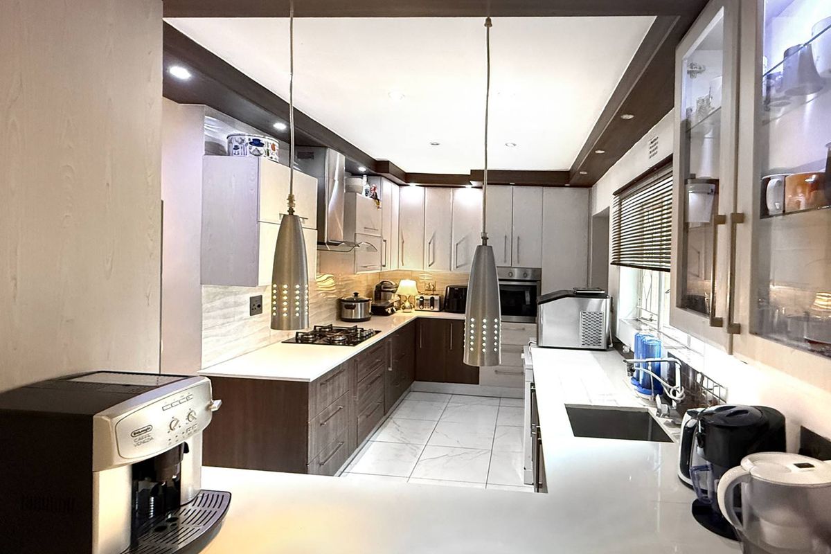 Modern kitchen featuring two-tone cabinetry, stone countertops, integrated oven, gas hob, extractor fan, and tiled flooring with recessed ceiling lighting.