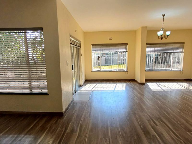 Spacious, light-filled living area featuring modern laminate flooring, large windows with fitted blinds, and direct access to the exterior via a sliding glass door.