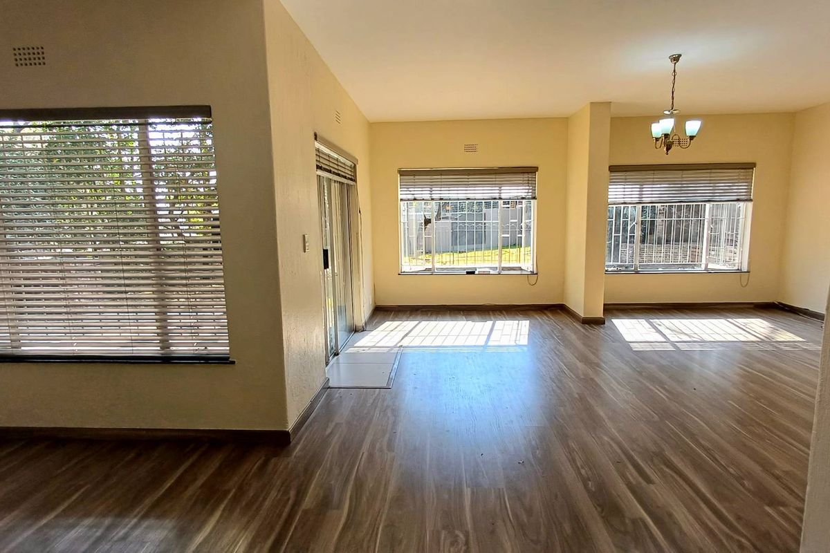 Spacious, light-filled living area featuring modern laminate flooring, large windows with fitted blinds, and direct access to the exterior via a sliding glass door.
