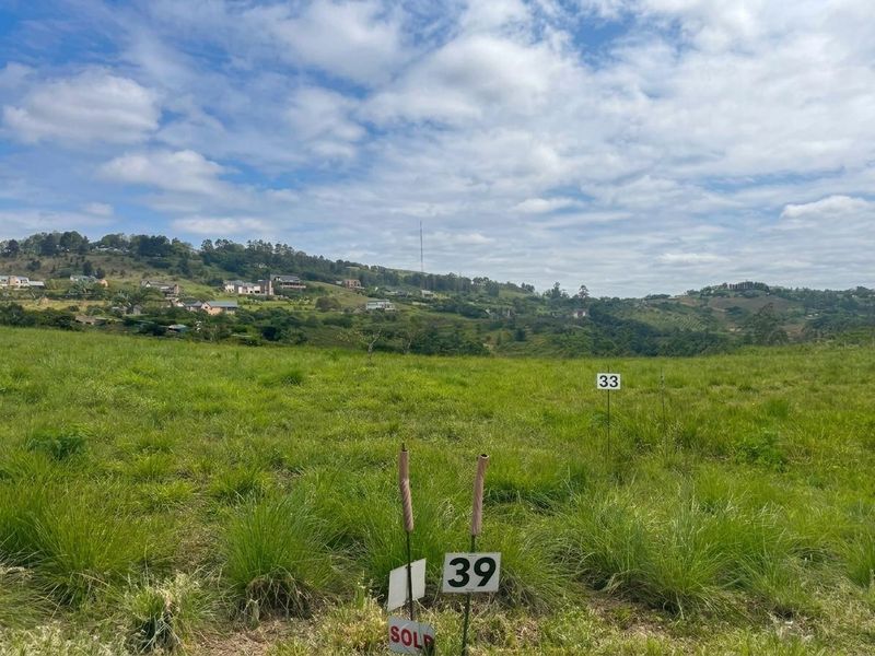 A view of a vacant residential plot featuring grassy terrain and boundary markers, set against a scenic hillside landscape.