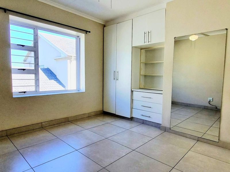 A bright, empty bedroom featuring neutral tiled flooring, built-in white cabinetry with integrated shelving, and a large wall-mounted mirror.