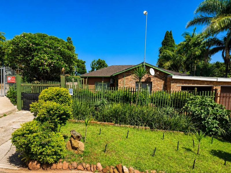 Front view of a brick cottage featuring a tiled roof, secure metal fencing, a driveway, and a garage.