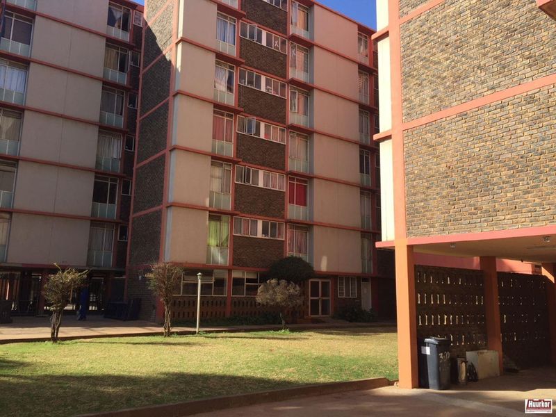 Exterior view of a multi-story apartment complex featuring brick and concrete facade with a shared communal garden area.